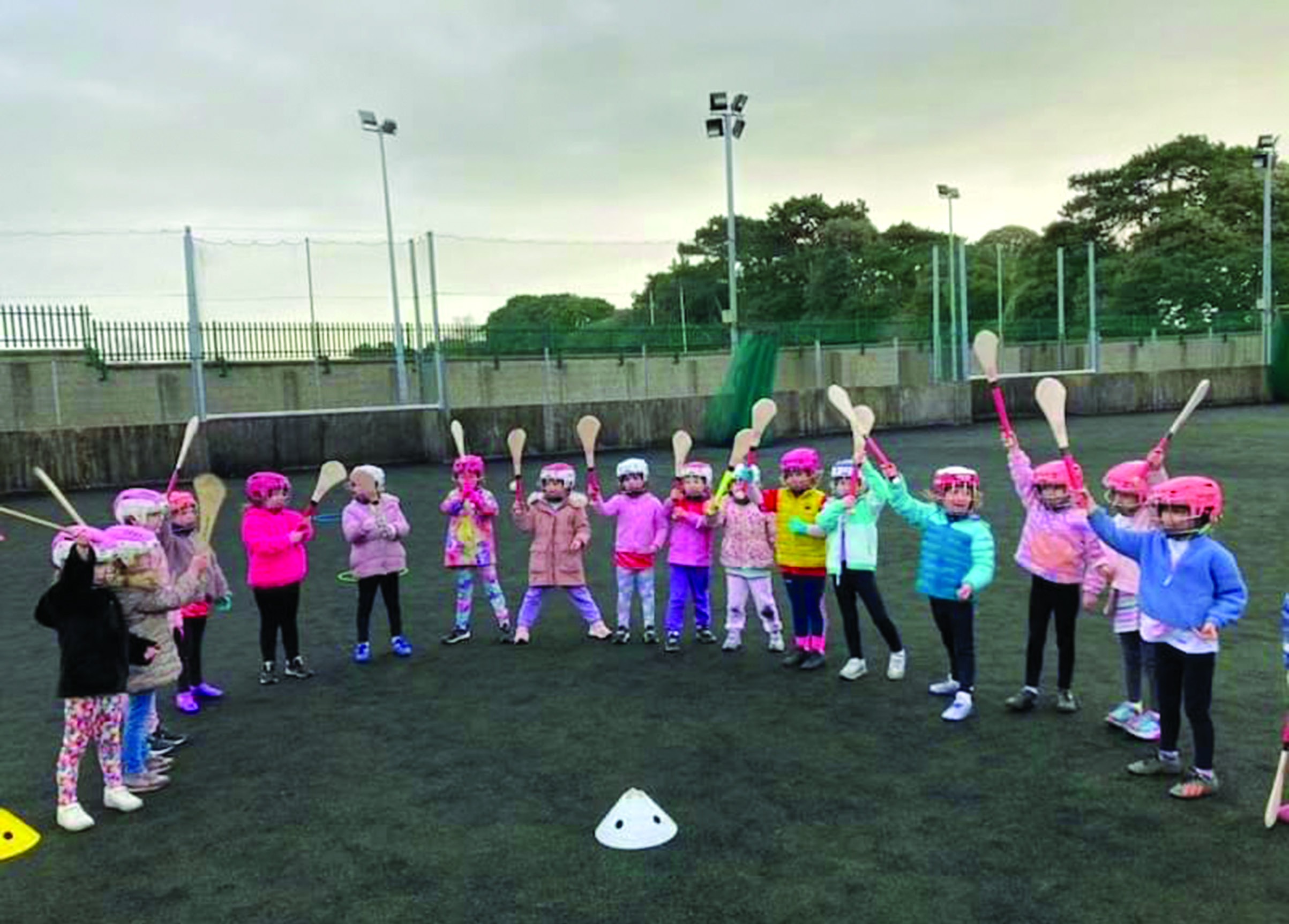 Nursery camogie group holding hurls aloft on the astro pitch